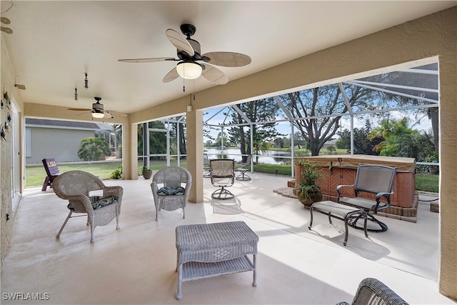 view of patio / terrace with a hot tub, glass enclosure, a water view, and ceiling fan