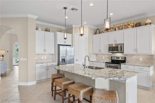 kitchen featuring stainless steel appliances, an island with sink, pendant lighting, sink, and white cabinetry