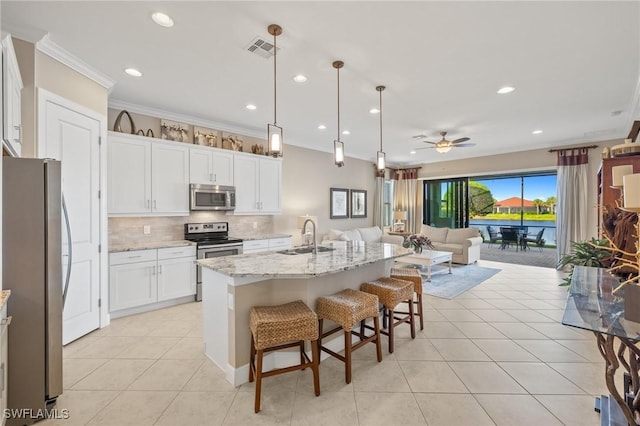 kitchen featuring hanging light fixtures, stainless steel appliances, a center island with sink, white cabinets, and ceiling fan