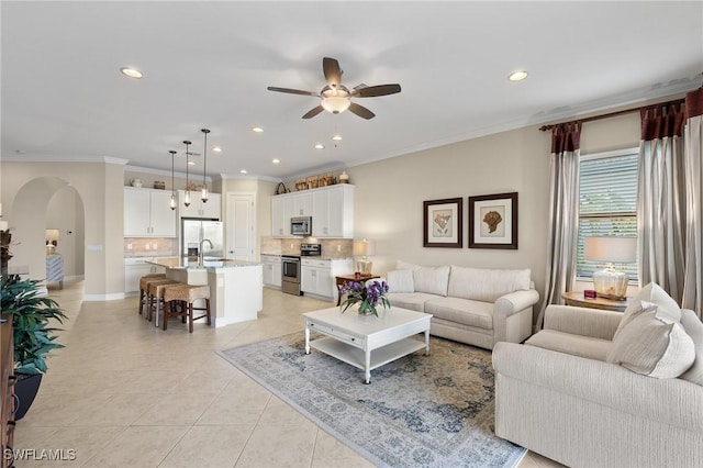 tiled living room with ceiling fan, ornamental molding, and sink