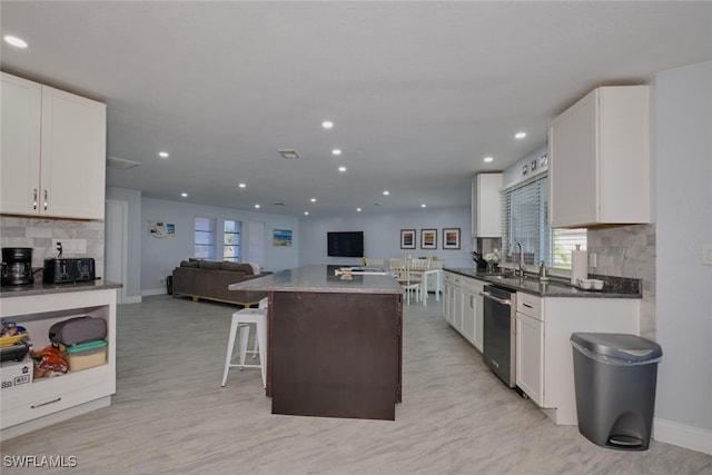 kitchen featuring stainless steel dishwasher, white cabinetry, a breakfast bar area, and tasteful backsplash