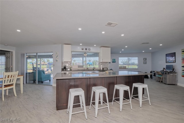 kitchen with sink, a kitchen island, backsplash, white cabinets, and a breakfast bar