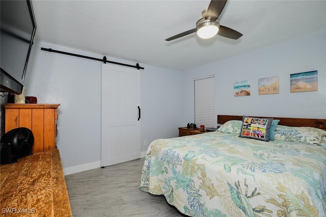 bedroom with ceiling fan, light hardwood / wood-style flooring, and a barn door