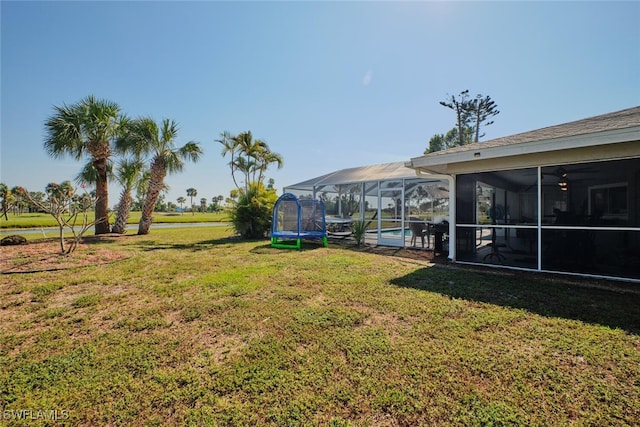 view of yard featuring a trampoline, a sunroom, and glass enclosure