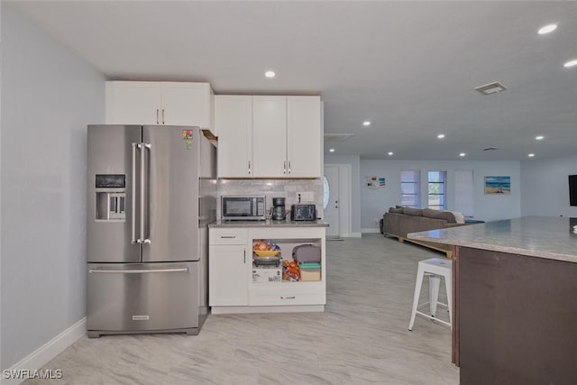 kitchen featuring white cabinets, tasteful backsplash, stainless steel appliances, and a kitchen bar