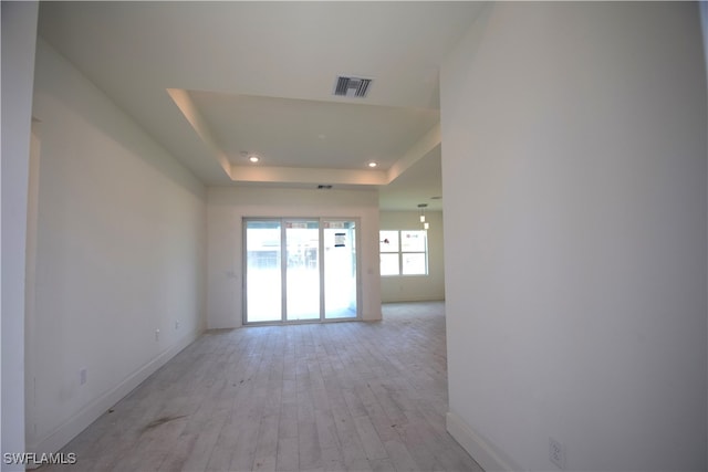 spare room with a tray ceiling and light wood-type flooring