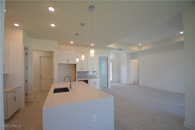 kitchen with an island with sink, light hardwood / wood-style flooring, sink, pendant lighting, and white cabinets