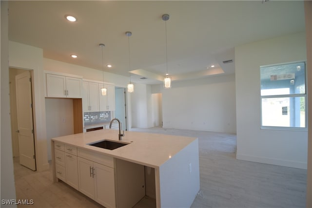 kitchen featuring decorative backsplash, hanging light fixtures, a center island with sink, sink, and white cabinetry