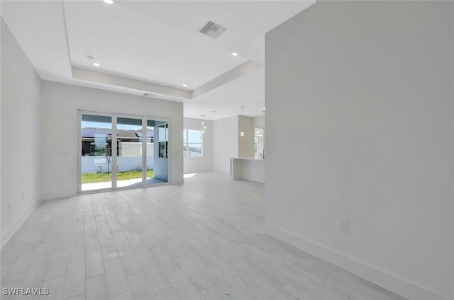 empty room featuring visible vents, baseboards, a tray ceiling, recessed lighting, and light wood-style flooring