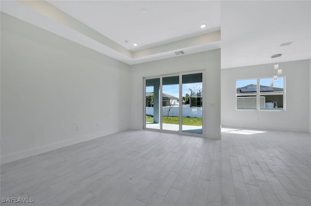 empty room featuring a tray ceiling, wood finished floors, visible vents, and baseboards