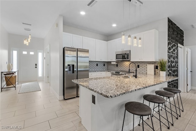 kitchen with appliances with stainless steel finishes, sink, kitchen peninsula, hanging light fixtures, and white cabinets