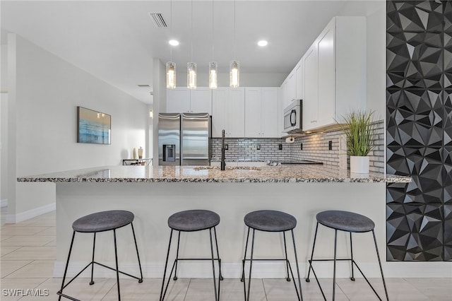 kitchen featuring a kitchen breakfast bar, stainless steel appliances, sink, light stone countertops, and white cabinetry