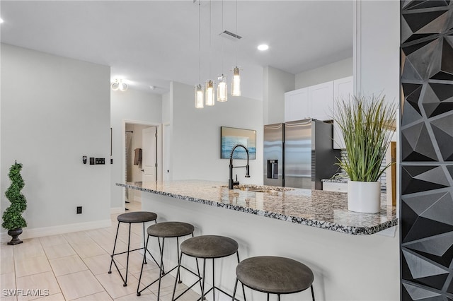 kitchen featuring white cabinets, stainless steel fridge with ice dispenser, stone countertops, pendant lighting, and sink