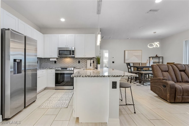 kitchen with white cabinetry, light stone countertops, appliances with stainless steel finishes, and hanging light fixtures