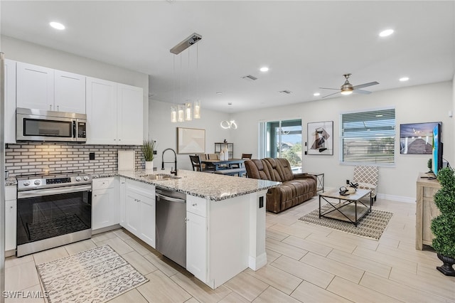 kitchen with kitchen peninsula, white cabinets, appliances with stainless steel finishes, pendant lighting, and sink