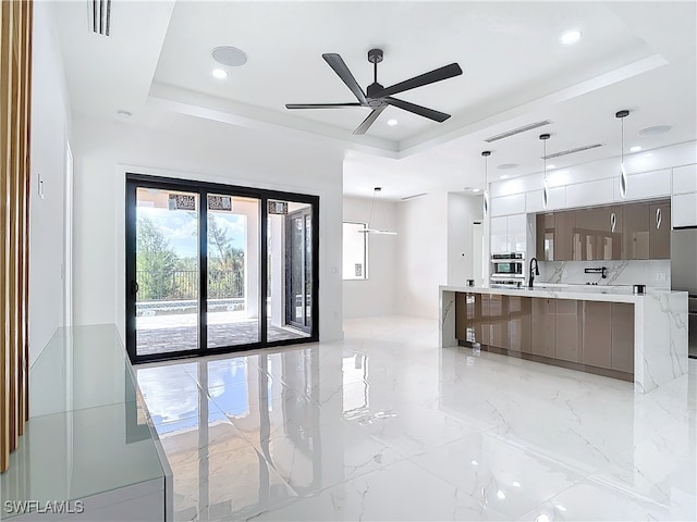 kitchen featuring a tray ceiling, ceiling fan, sink, and decorative light fixtures