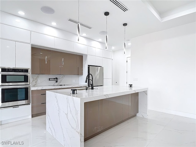 kitchen with pendant lighting, backsplash, a large island with sink, light stone countertops, and appliances with stainless steel finishes