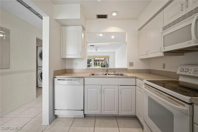 kitchen with white appliances, sink, stacked washer and dryer, white cabinetry, and light tile patterned flooring