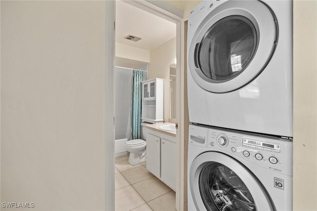 clothes washing area with light tile patterned flooring and stacked washer and dryer