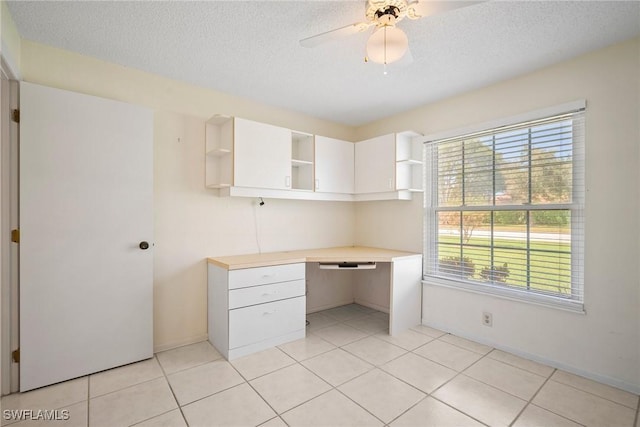 unfurnished office featuring light tile patterned floors, built in desk, ceiling fan, and a healthy amount of sunlight