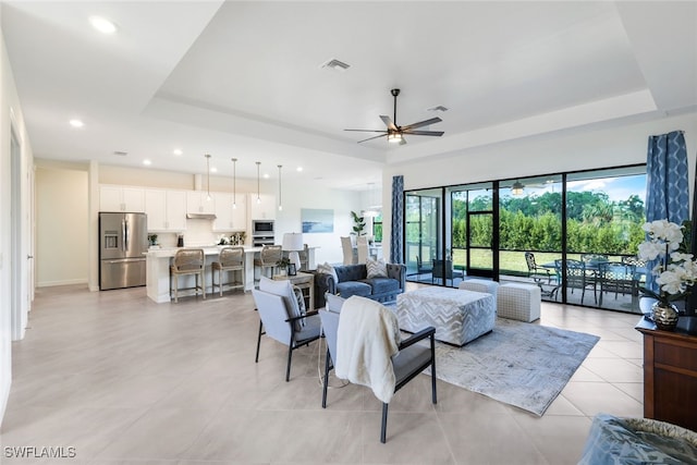 tiled living room with ceiling fan and a raised ceiling