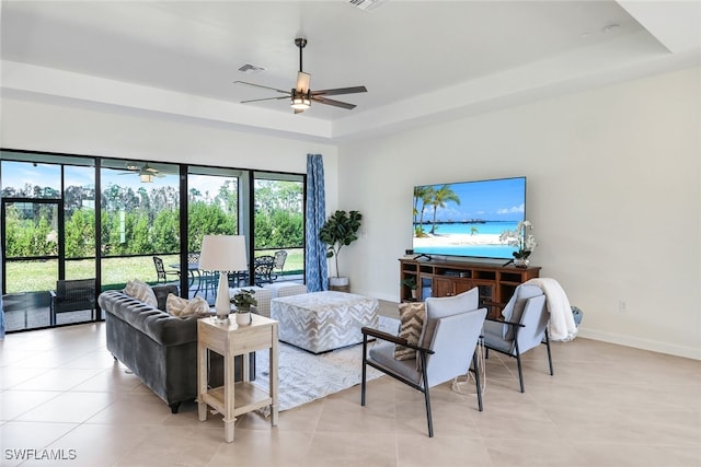 living room with ceiling fan, a tray ceiling, and light tile patterned floors