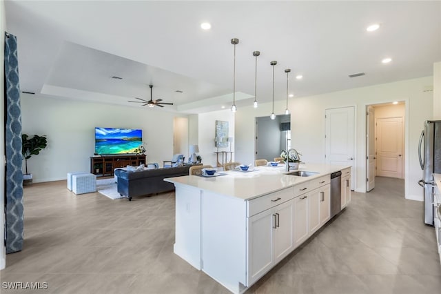 kitchen featuring sink, hanging light fixtures, ceiling fan, white cabinets, and a center island with sink