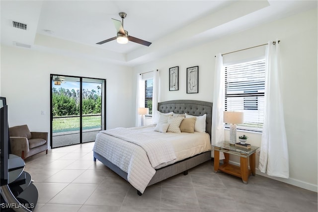 tiled bedroom with ceiling fan, a tray ceiling, access to outside, and multiple windows