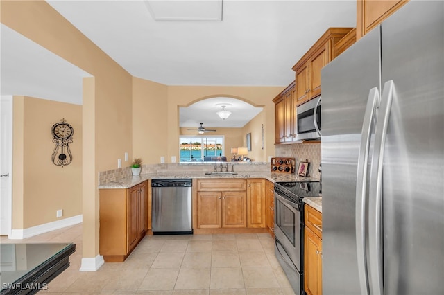 kitchen featuring light stone countertops, ceiling fan, kitchen peninsula, light tile patterned floors, and appliances with stainless steel finishes