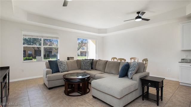 living room featuring ceiling fan, a raised ceiling, and light tile patterned floors