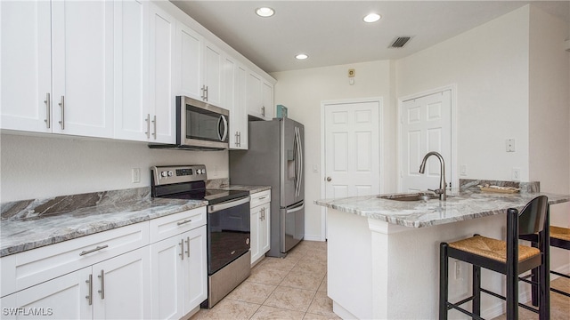 kitchen with sink, white cabinetry, stainless steel appliances, light stone counters, and a kitchen bar