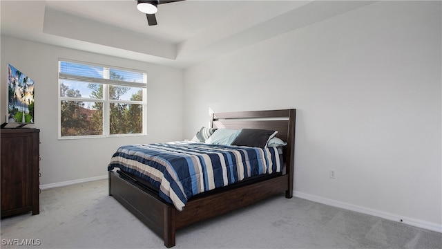 bedroom featuring ceiling fan, light colored carpet, and a raised ceiling