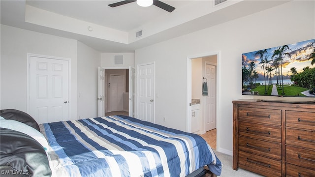 carpeted bedroom featuring ensuite bath, a raised ceiling, and ceiling fan