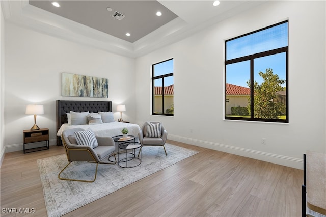 bedroom featuring light hardwood / wood-style floors, a raised ceiling, and multiple windows