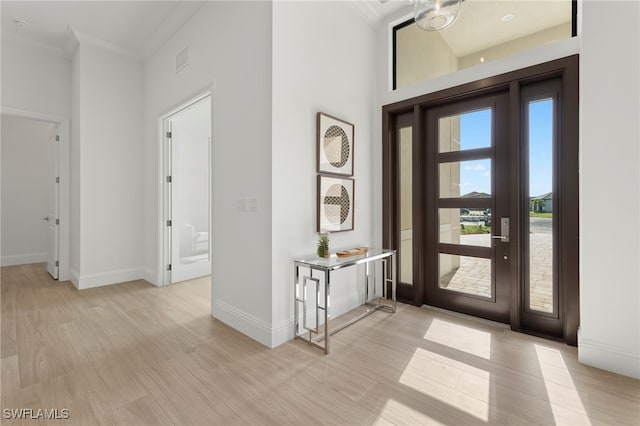 foyer featuring light hardwood / wood-style floors, a high ceiling, and ornamental molding