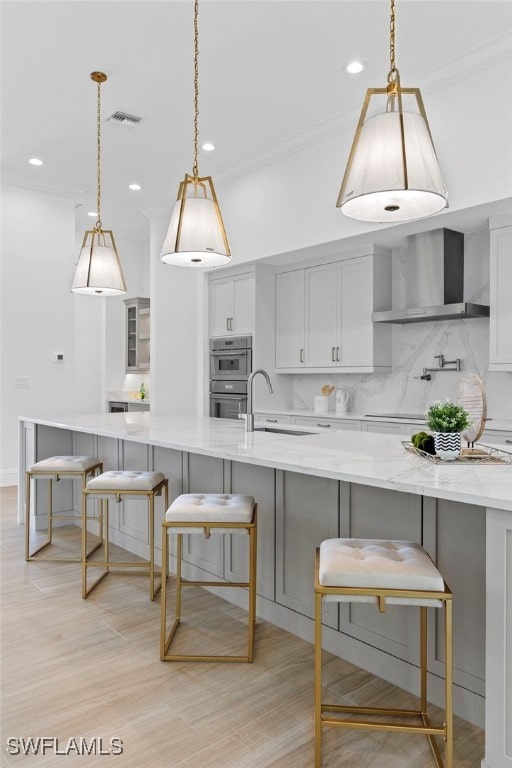 kitchen with light stone countertops, a breakfast bar, light hardwood / wood-style floors, and wall chimney exhaust hood