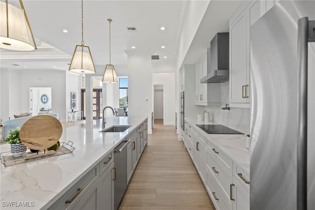 kitchen featuring light stone countertops, wall chimney exhaust hood, stainless steel appliances, sink, and hanging light fixtures