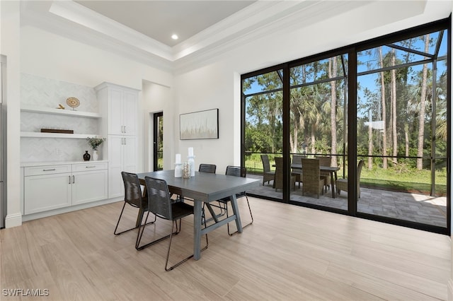 dining room featuring a high ceiling, a tray ceiling, light hardwood / wood-style flooring, and ornamental molding