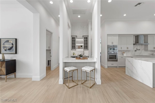 kitchen featuring light hardwood / wood-style floors, wall chimney range hood, backsplash, and double oven