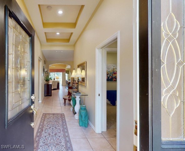 5291 Laurel Oak Ct, North Port, FL 34287 - hall featuring baseboards, arched walkways, light tile patterned floors, and a tray ceiling