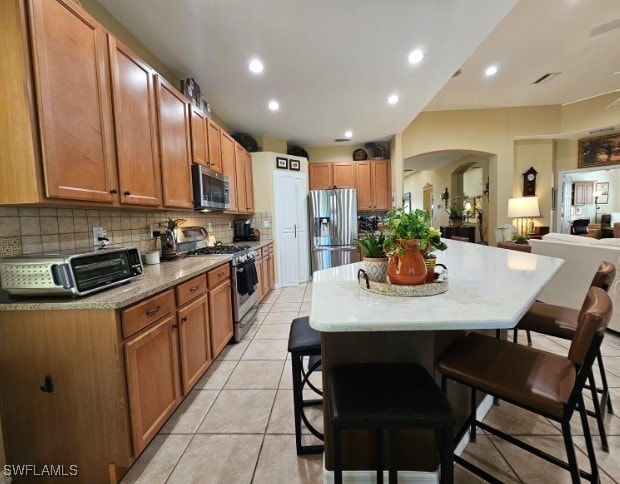 kitchen with tasteful backsplash, light tile patterned floors, a kitchen breakfast bar, stainless steel appliances, and a center island