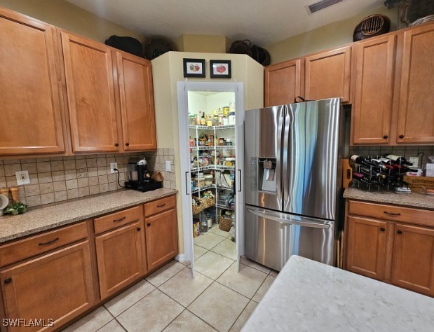 kitchen with light stone countertops, decorative backsplash, light tile patterned flooring, and stainless steel fridge