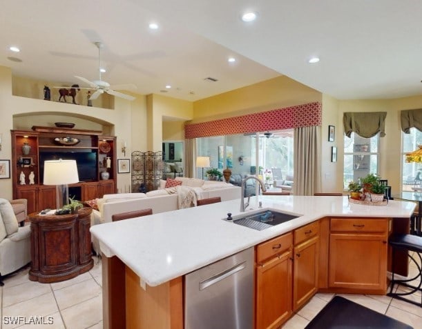 kitchen with sink, an island with sink, ceiling fan, stainless steel dishwasher, and light tile patterned floors