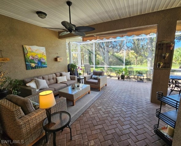 view of patio featuring an outdoor living space, glass enclosure, and ceiling fan