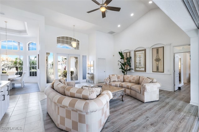 living room featuring light hardwood / wood-style flooring, high vaulted ceiling, and ceiling fan with notable chandelier