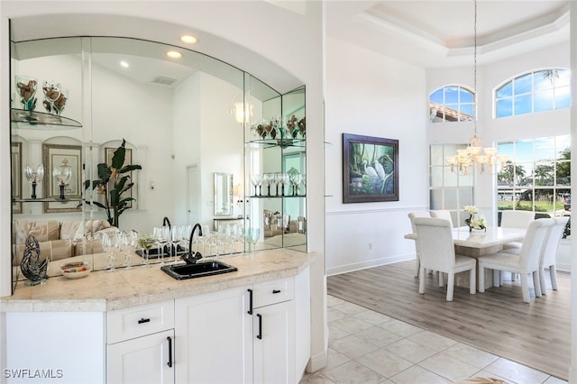 kitchen featuring sink, white cabinetry, pendant lighting, light hardwood / wood-style flooring, and a chandelier