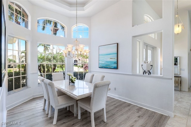 dining area with a wealth of natural light, a high ceiling, an inviting chandelier, and light hardwood / wood-style floors