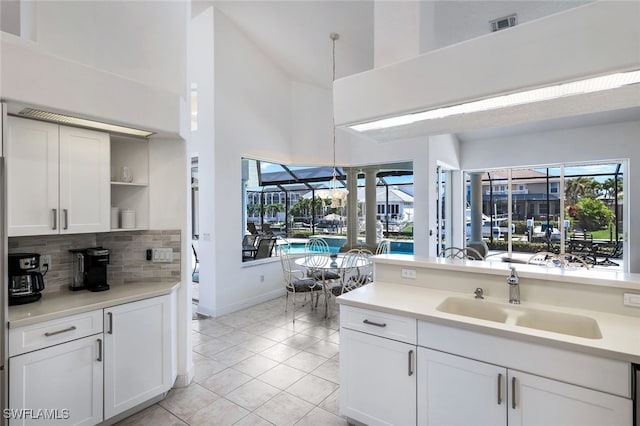 kitchen featuring a high ceiling, sink, light tile patterned flooring, pendant lighting, and white cabinetry