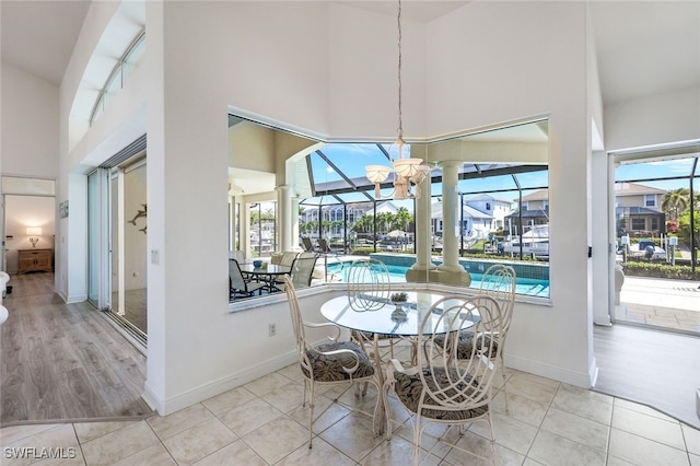 dining area with a wealth of natural light, an inviting chandelier, a towering ceiling, and light hardwood / wood-style floors