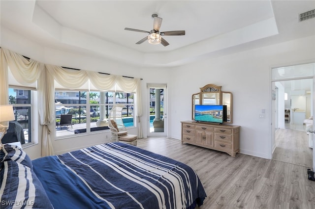 bedroom with access to outside, a tray ceiling, light wood-type flooring, and ceiling fan